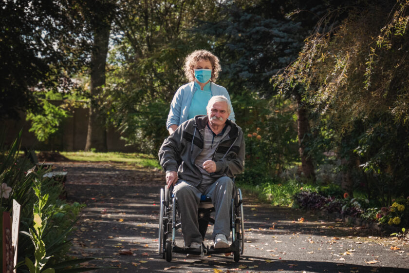 Zdjęcie pielęgniarki, która wybrała się na spacer z pacjentem na wózku inwalidzkim.