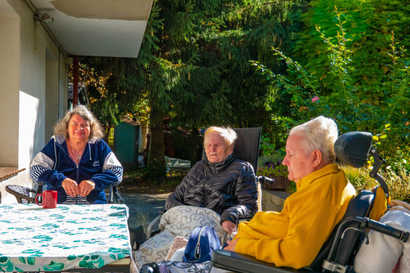 Zdjęcie trzech starszych kobiet, które siedzą przy stoliku w ogrodzie