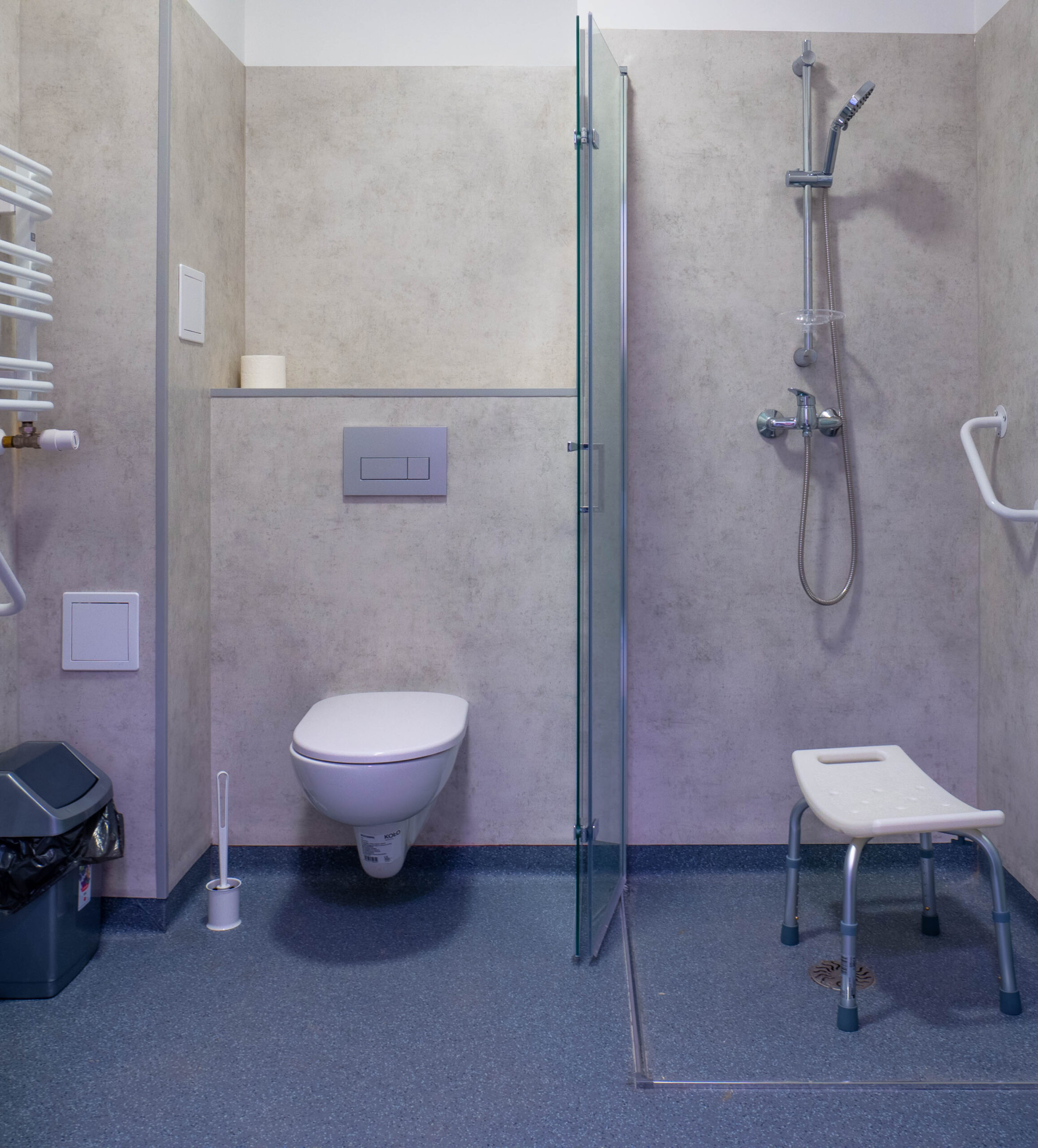 Zdjęcie łazienki w Warszawskim Domu Seniora. Na zdjęciu widać sedes, prysznic i specjalną ławeczkę ułatwiającą kąpiel.