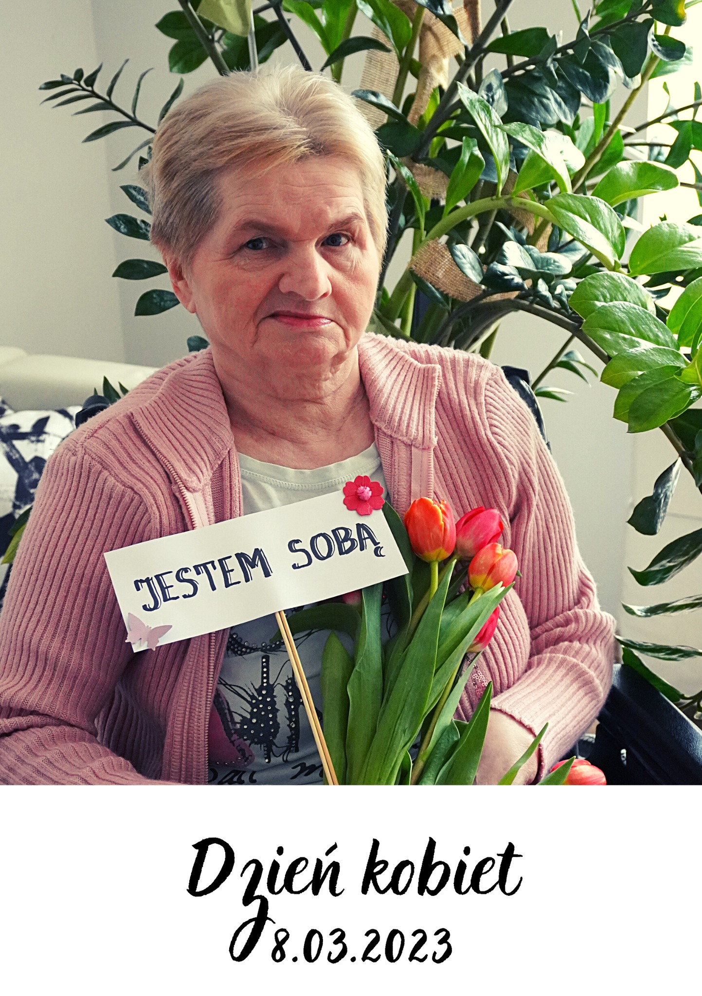 Zdjęcie starsze Pani z kwiatami, która trzyma tabliczkę z napisem "Jestem sobą".