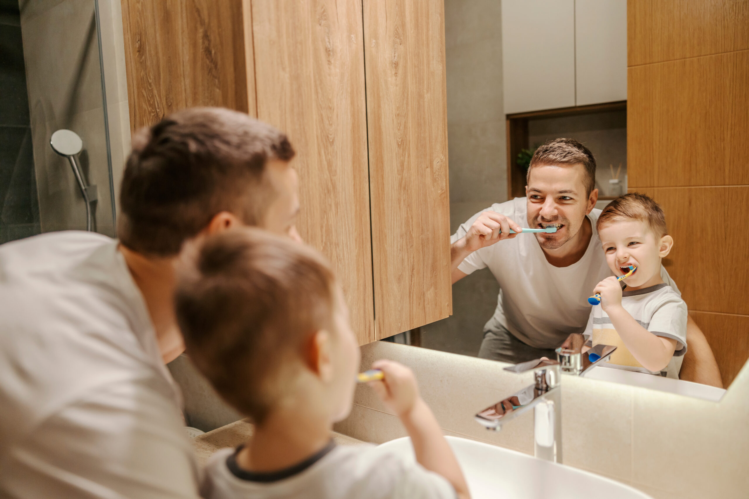 Zdjęcie taty i syna, którzy wspólnie przed lustrem myją zęby.