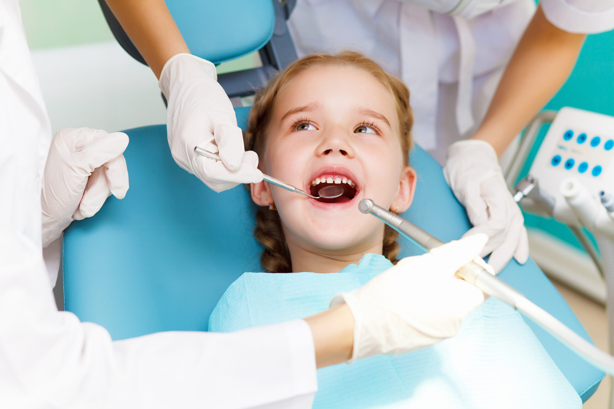 Zdjęcie dziewczynki na fotelu dentystycznym z otwartą buzią. Dentystka za pomocą lusterka ogląda zęby.