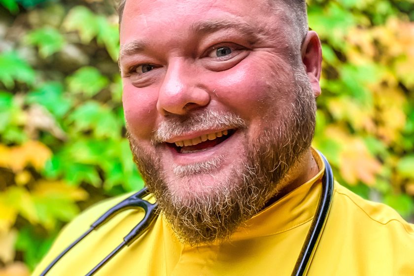 Zdjęcie obrazuje uśmiechającego się lekarza w żółtym stroju