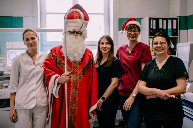 Fotografia przedstawia grupę osób, cztery kobiety i jednego mężczyznę przebranego w strój Świętego Mikołaja. Wszystkie osoby uśmiechają się, jedna z kobiet ma założoną czapkę Mikołaja, wszystkie osoby pozują do zdjęcia w laboratorium szpitalnym.