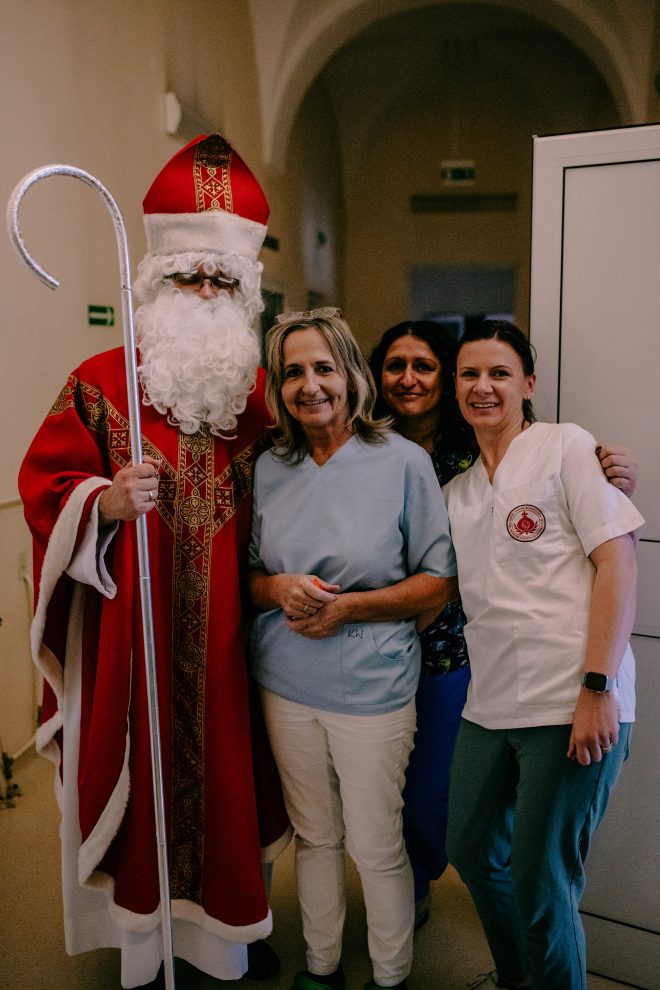 Fotografia przedstawia grupę osób, trzy kobiety i jednego mężczyznę przebranego w strój Świętego Mikołaja. Wszystkie osoby uśmiechają się, pozując do zdjęcia w korytarzu szpitalnym