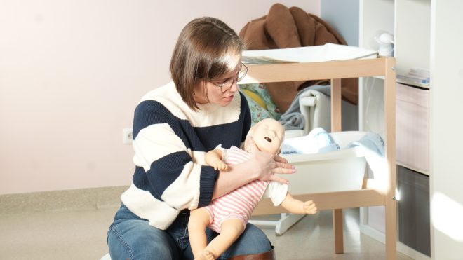Zdjęcie przedstawia kobietę siedzącą w gabinecie z fantomem noworodka