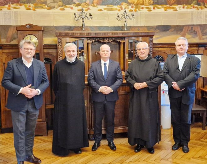 Fotografia przedstawia grupę pięciu mężczyzn stojących obok siebie w dużym pomieszczeniu. Wśród mężczyzn jest też dwóch braci zakonnych.