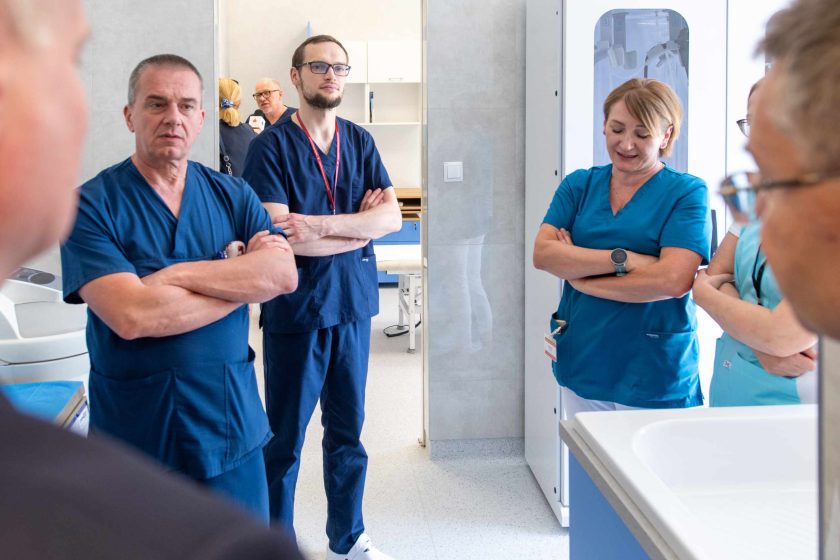 Zdjęcie przedstawia grupę personelu medycznego stojącą obok siebie w dużym pomieszczeniu medycznym