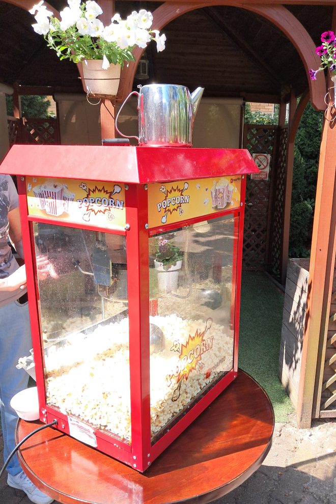 Zdjęcie przedstawia dużą maszynę do popcornu stojącą na okrągłym stoliku w ogrodzie