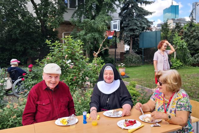 Zdjęcie przedstawia seniorów oraz siostrę zakonną, którzy uczestniczą w pikniku plenerowym
