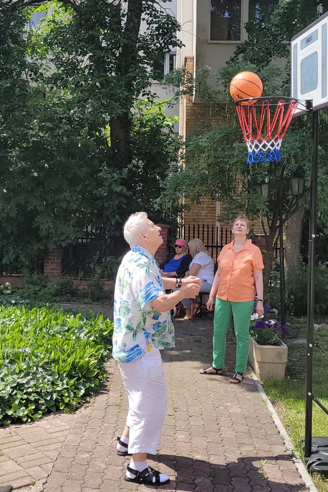 Zdjęcie przedstawia starszego mężczyznę grającego w koszykówkę w ogrodzie