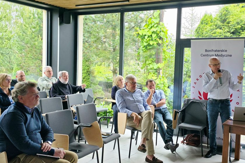 Fotografia przedstawia osoby uczestniczące w zebraniu - konferencji, znajdujące się w dużym, jasnym pomieszczeniu.