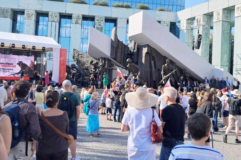 Fotografia przedstawia grupę osób znajdującą się przed pomnikiem Powstańców Warszawskich