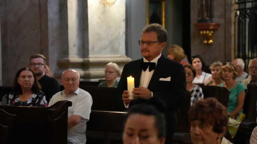 Fotografia przedstawia grupę osób znajdującą się w dużym kościele. Osoby te siedzą lub stoją w ławach kościelnych.