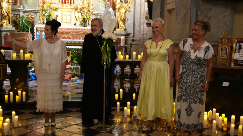 Publiczność w kościele stoi i bije brawa. Wszyscy wyglądają na zadowolonych, niektórzy się uśmiechają.