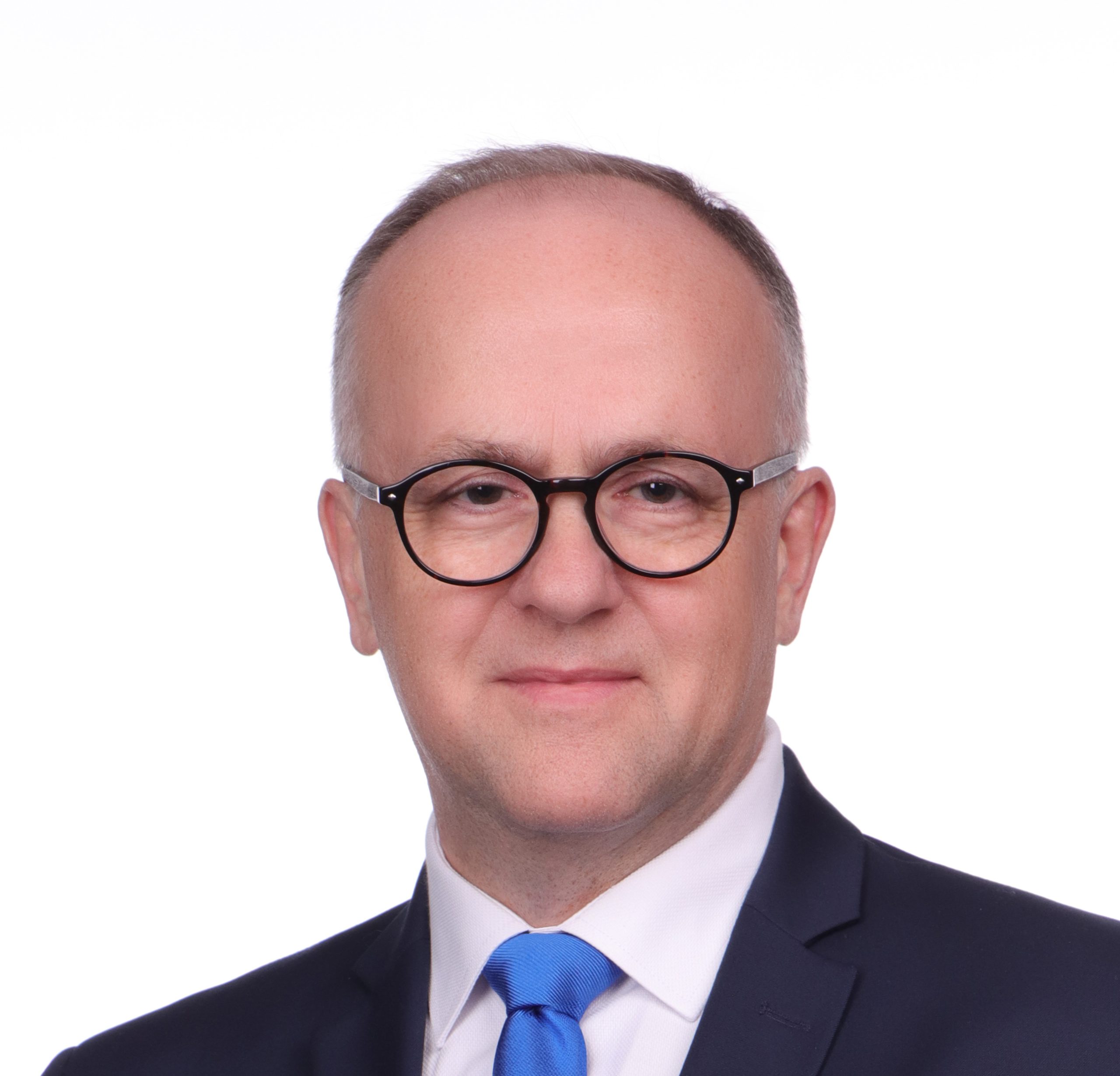 Fotografia przedstawia mężczyznę w średnim wieku, w okularach i garniturze.