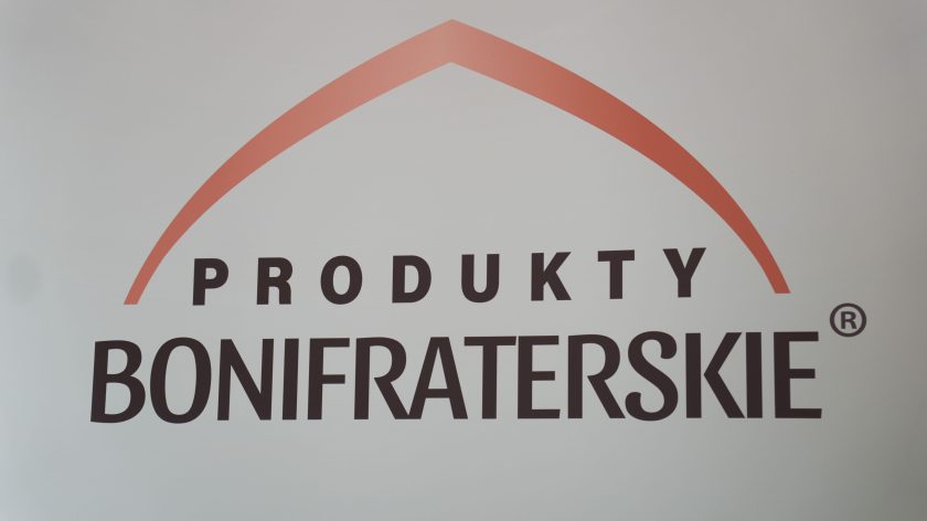 Zbliżenie na logo „Produkty Bonifraterskie”, umieszczone na jasnym tle, z charakterystycznym łukiem w kolorze czerwonym. Logo jest minimalistyczne i nowoczesne