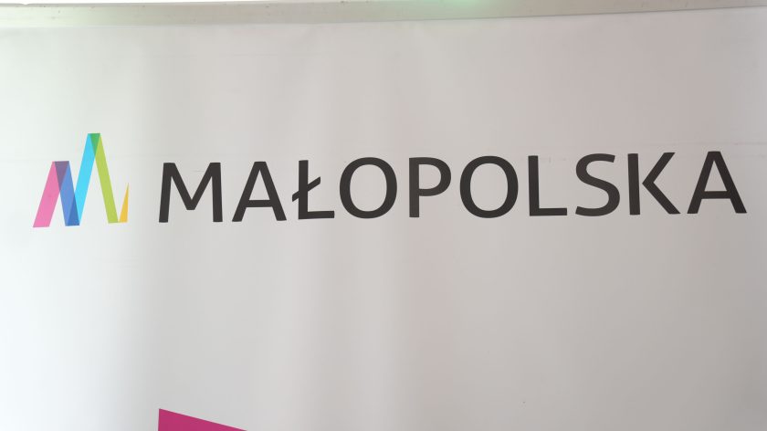 Baner promujący „Małopolska” na białym tle z wielobarwnym logotypem w kształcie litery „M”. Baner prezentuje prosty, elegancki design