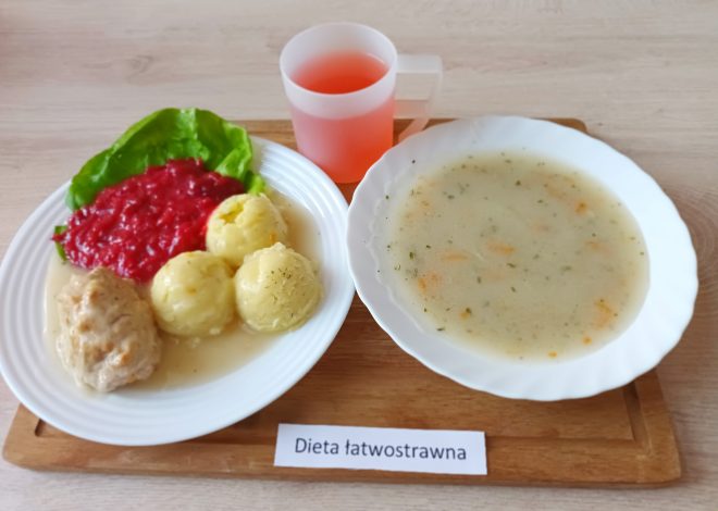 Na drewnianej tacy znajduje się zestaw obiadowy oznaczony jako "Dieta łatwostrawna". Na talerzu obiadowym ułożone są: trzy ziemniaczane kluski polane sosem, kotlet mielony w sosie, liść sałaty i porcja buraczków zasmażanych. Obok stoi miseczka z jasną zupą, w której widać kawałki warzyw. Na tacy znajduje się również plastikowy kubek z czerwonym napojem, przypominającym kompot