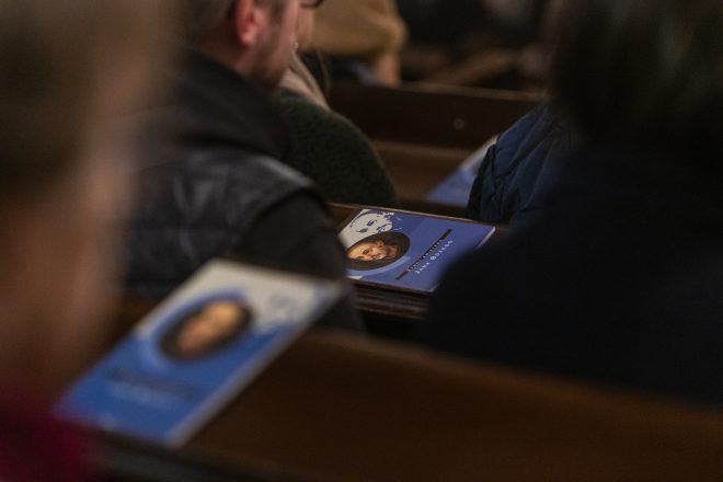 Zbliżenie na książeczki leżące na ławkach kościelnych. Na okładce wizerunek duchownego oraz napis wskazujący na temat przewodni uroczystości