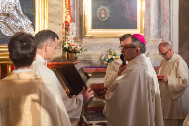 Zbliżenie na biskupa z mitrą, który składa modlitwę przed obrazem św. Bonifacego, wspierany przez asystujących mu kapłanów