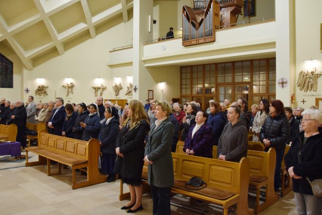 Wierni zgromadzeni w zabytkowym kościele o bogato zdobionych wnętrzach uczestniczą w uroczystej liturgii. Część z nich to duchowni i zakonnice, a wśród zgromadzonych widoczne są osoby starsze i młodsze, skupione na modlitwie