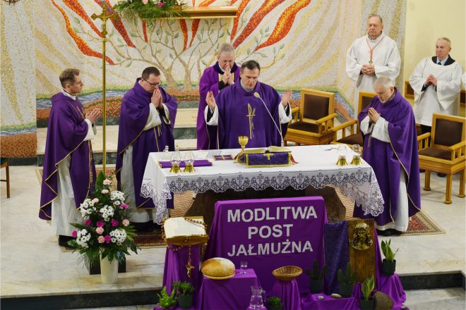 Moment Mszy Świętej, w którym kapłan wznosi ręce w geście modlitwy. Ołtarz udekorowany jest fioletową tkaniną z napisem „MODLITWA, POST, JAŁMUŻNA”. Przed ołtarzem widoczne są chleb, dzban z wodą i rośliny jako symbole postu i jałmużny