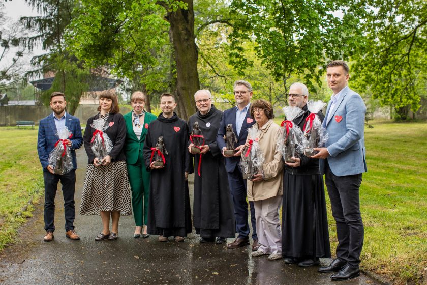 Wspólne zdjęcie laureatów nagród – Grupa dziesięciu osób – przedstawicieli zakonu, instytucji i zaproszonych gości – pozuje na tle drzew, trzymając statuetki Bonifraterskie opakowane w celofan z czerwoną wstążką