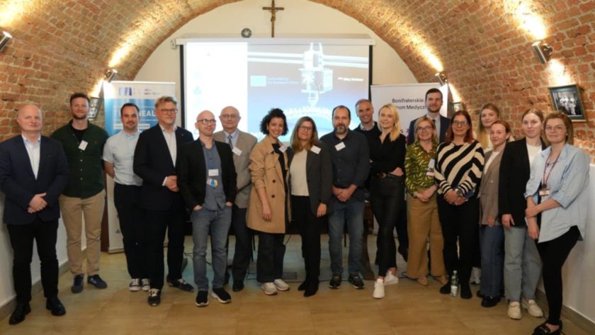 Uczestnicy międzynarodowego projektu Erasmus+ TECHHEALTH zgromadzeni na wspólnym zdjęciu w sali konferencyjnej Bonifraterskiego Centrum Medycznego. Uśmiechnięte twarze, tło stanowią prezentacja multimedialna oraz banery promujące projekt