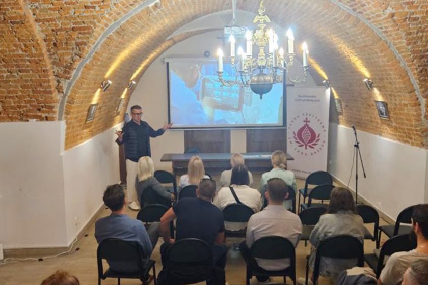 Prelegent prowadzi wykład w sali z ceglanym sklepieniem, prezentując nowoczesne technologie medyczne uczestnikom spotkania Bonifraterskiego Centrum Medycznego.