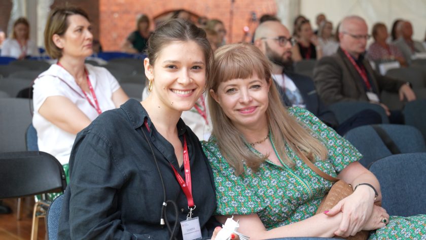 wie uczestniczki konferencji uśmiechają się do obiektywu, siedząc wśród publiczności wydarzenia Bonifraterskich Spotkań z Rehabilitacją.