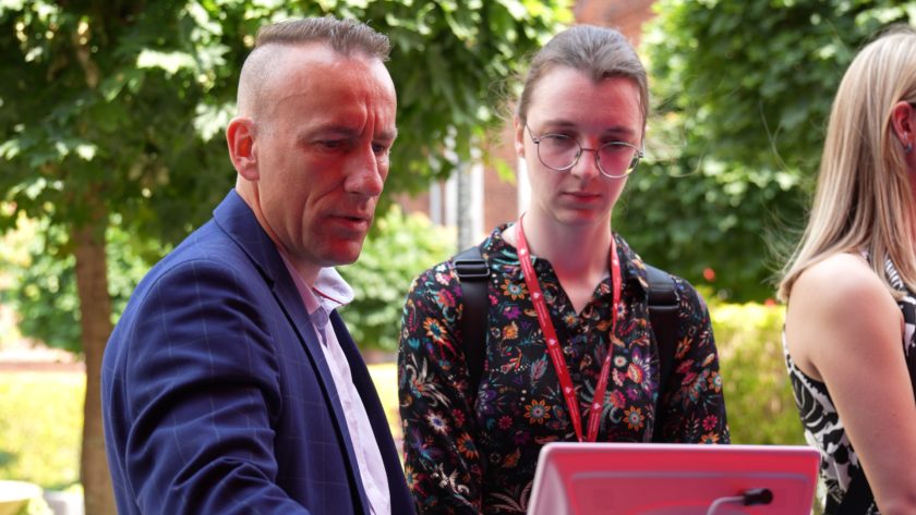 Zbliżenie na mężczyznę w garniturze, który prezentuje urządzenie medyczne młodej kobiecie w okularach i kwiecistej sukience.