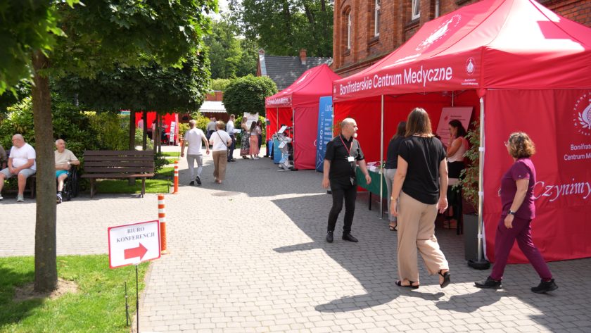 Widok ogólny alei wystawowej z czerwonymi namiotami Bonifraterskiego Centrum Medycznego i uczestnikami poruszającymi się w kierunku stoisk.