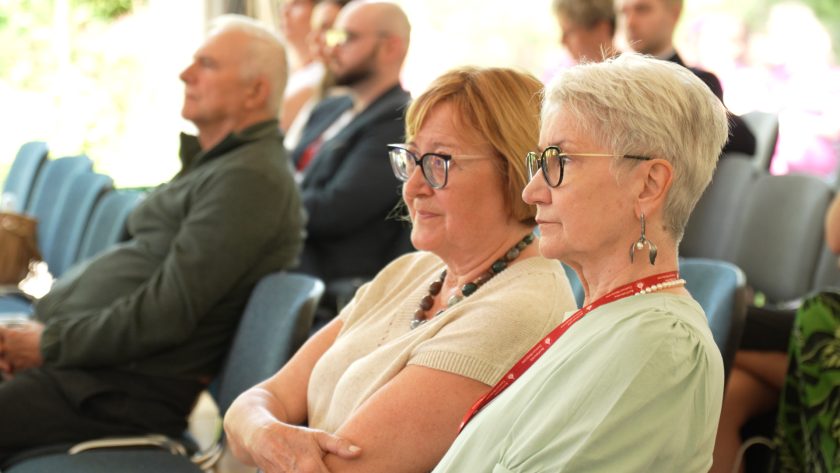 Dwie starsze kobiety siedzące w pierwszym rzędzie na konferencji, uważnie słuchające wystąpienia.