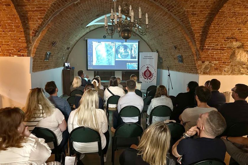 Publiczność uczestniczy w wykładzie z prezentacją obrazów medycznych w historycznej sali konferencyjnej Bonifraterskiego Centrum Medycznego.