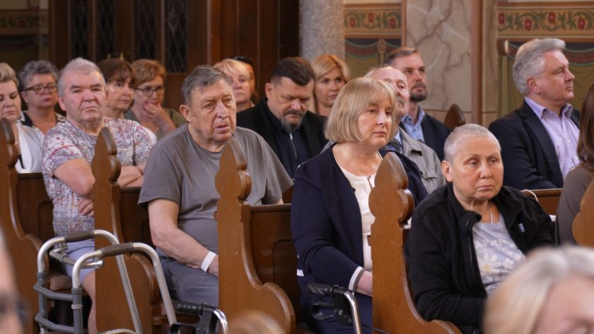 Wierni, w tym osoby starsze oraz pacjenci, siedzą skupieni podczas nabożeństwa w kościele.