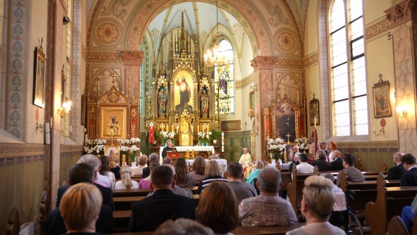Panorama wnętrza kościoła z widokiem na ołtarz, wiernych oraz piękne malowidła i witraże.