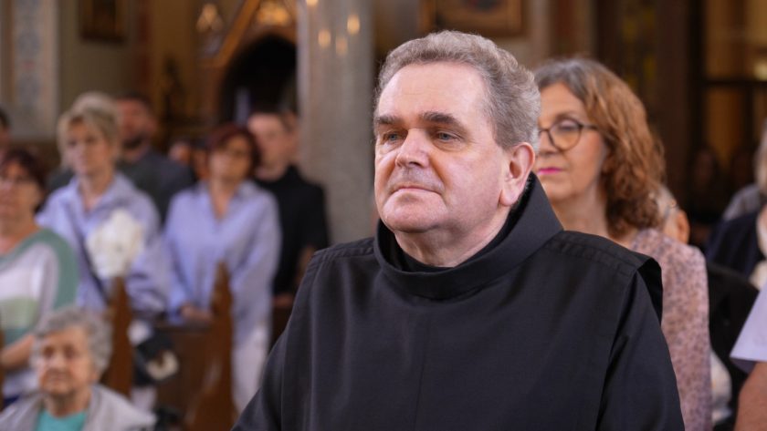 Starszy brat zakonny z powagą uczestniczy w liturgii, stojąc w nawie głównej kościoła.