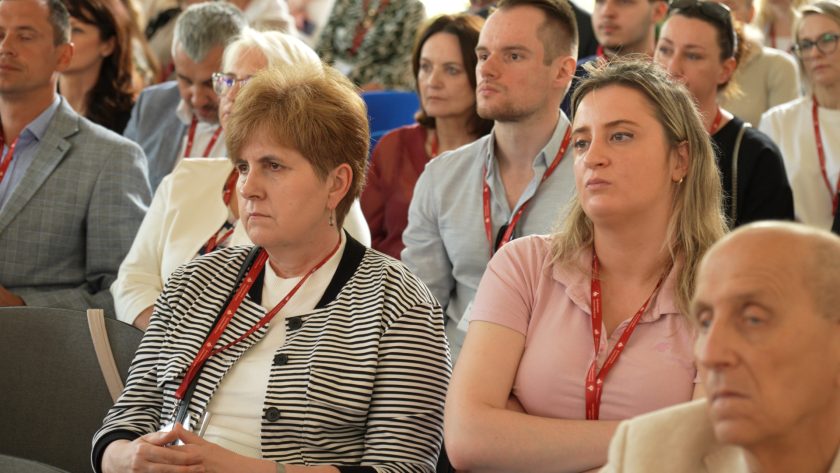 Uczestnicy konferencji z uwagą słuchają prelekcji. Na pierwszym planie dwie kobiety i mężczyzna z identyfikatorami Bonifraterskiego Centrum Medycznego.