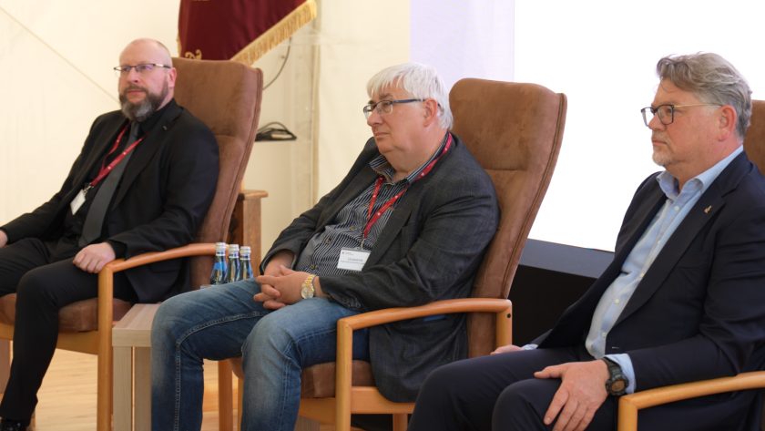 Trzech ekspertów zasiadających w fotelach podczas panelu dyskusyjnego, wsłuchanych w przebieg rozmowy.