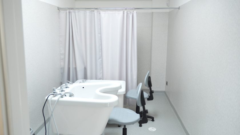 Widok ogólny pomieszczenia do hydroterapii w Bonifraterskim Centrum Medycznym, z wanną terapeutyczną i dwoma krzesłami ustawionymi za zasłoną zapewniającą prywatność pacjentom.