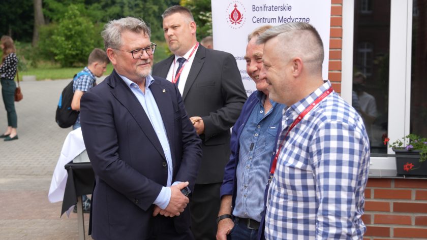 Rozmowy i uśmiechy uczestników wydarzenia na dziedzińcu dużego pomieszczenia, w tle baner z logotypem instytucji.