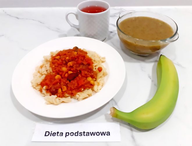 Talerz z makaronem świderki i sosem warzywnym z ciecierzycą i kukurydzą. Obok zupa kremowa, banan i filiżanka czerwonej herbaty. Dieta podstawowa