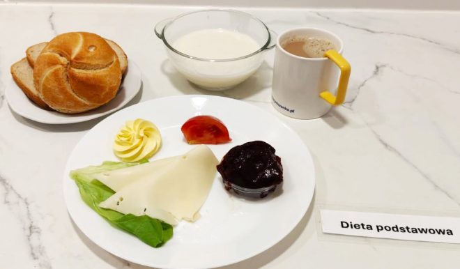 Lekki posiłek poranny: kromki pieczywa pszennego i żytniego, ser żółty, sałata z pomidorem, powidła śliwkowe, masło, miseczka mleka z płatkami oraz kubek kawy zbożowej z mlekiem