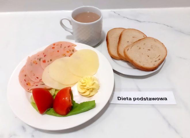 Talerz z plasterkami mortadeli z warzywami i sera żółtego, masło, pomidor i sałata. Obok trzy kromki chleba pszennego i filiżanka kawy z mlekiem. Dieta podstawowa