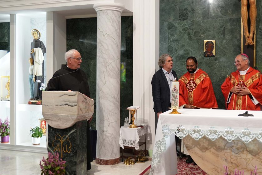Zakonnik w czarnym habicie przemawia z ambony, a po jego prawej stronie stoją brat Saji Mullankuzhy i biskup Michał Janocha, uśmiechnięci. W tle dekoracje ołtarza