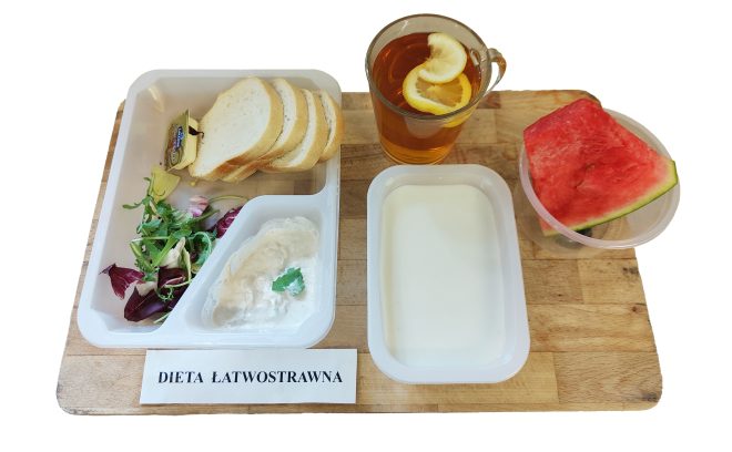 Jasne pieczywo z masłem i pastą twarogową, mieszanka sałat oraz herbata z cytryną. Dodatkowo galaretka mleczna i porcja arbuza. Zestaw prezentowany na tacy z napisem „Dieta łatwostrawna”