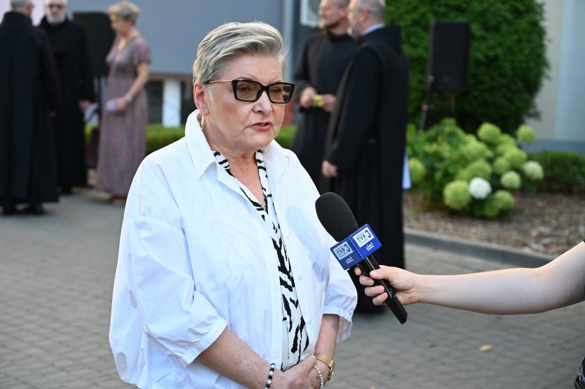 Kobieta w białej koszuli udziela wywiadu przed kamerą TVP3 Łódź podczas wydarzenia jubileuszowego Bonifratrów