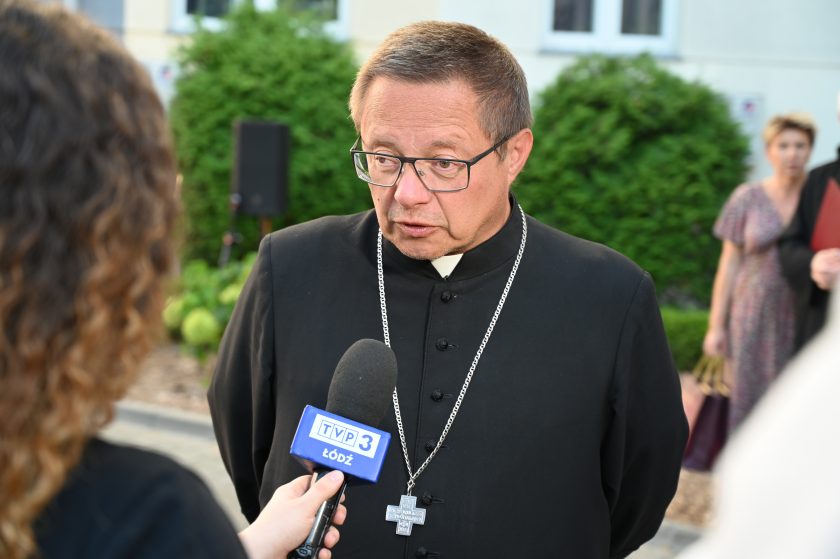 Biskup udziela wywiadu dziennikarce TVP3 Łódź. Widoczny mikrofon z logo stacji telewizyjnej