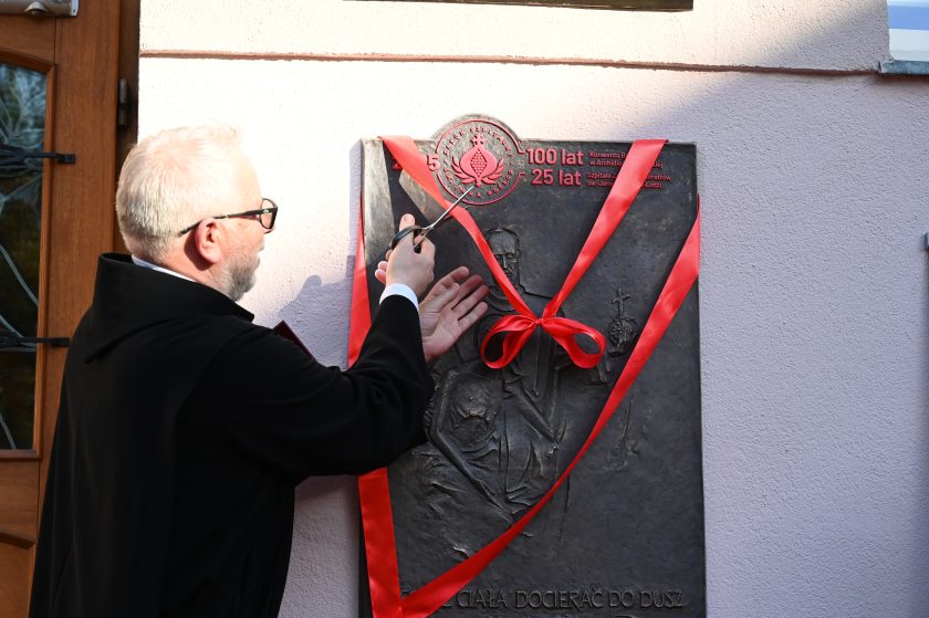 Zakonnik przecina czerwoną wstęgę podczas uroczystego odsłonięcia pamiątkowej tablicy jubileuszowej